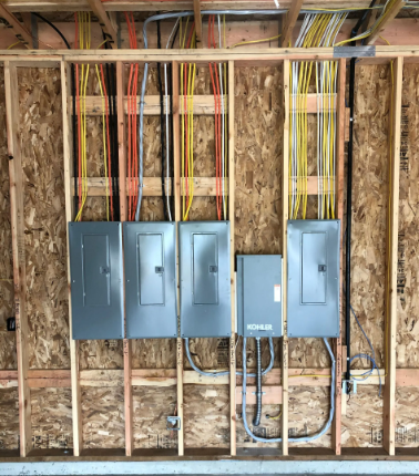 Electrical panels mounted on unfinished wall framing with exposed wiring in a construction area