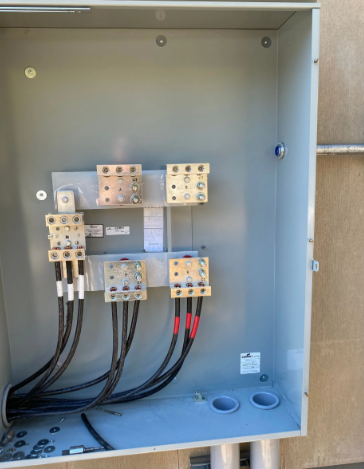 Open electrical panel with wiring, terminal blocks, and circuit connections inside a gray metal enclosure