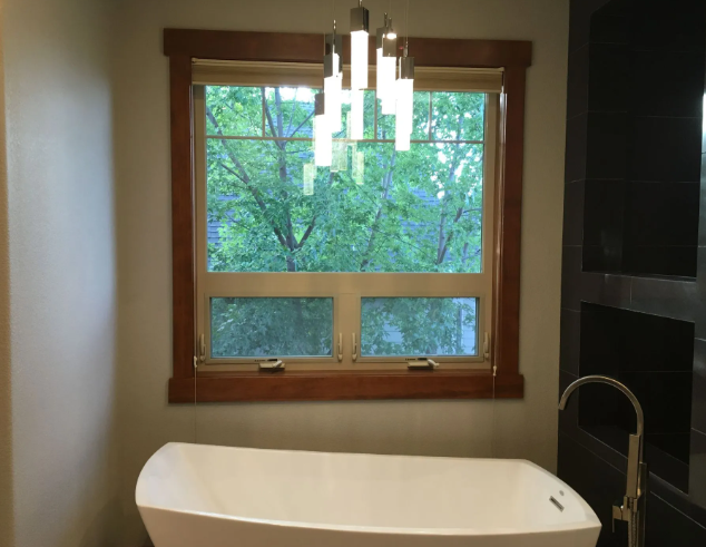 Modern bathroom with freestanding tub, wood-trimmed window, and pendant light fixtures