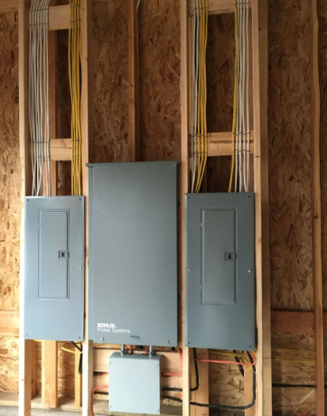 Three gray electrical breaker panels mounted on exposed wooden framing in a wall