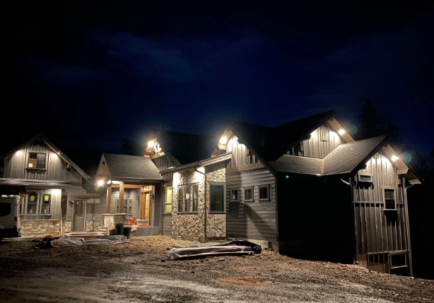 Nighttime exterior of a row of unfinished houses with porch lights and a rough dirt driveway