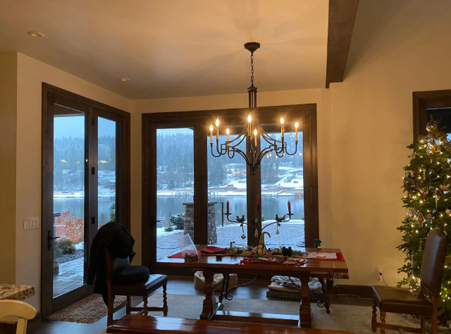 Cozy dining room with a wooden table, chandelier, and Christmas tree, overlooking a snowy outside view