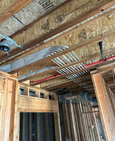 Exposed ceiling framing with wiring and ductwork above unfinished walls in a house under construction
