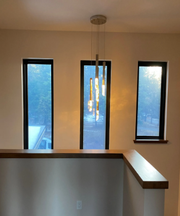 Modern interior landing with three narrow windows, a hanging light, and beige walls overlooking outdoors