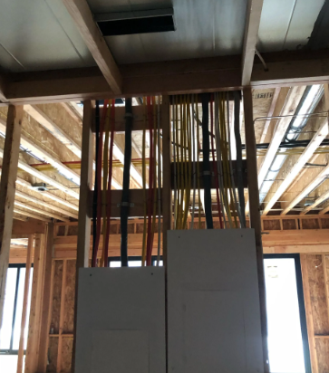 Exposed wooden framing in a building under construction, with vertical pipes or conduits centered above panels.