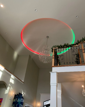 High-ceiling foyer with a chandelier and red-green LED-lit oval ceiling feature above a balcony.