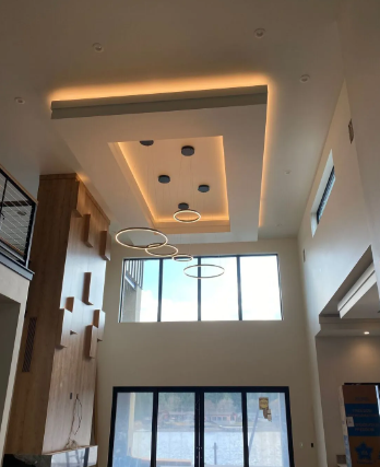 Modern lobby with high ceiling, warm recessed lighting, circular pendant lights, and tall windows.