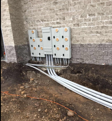 Electrical meter boxes mounted on a stone wall with white conduit running into the ground