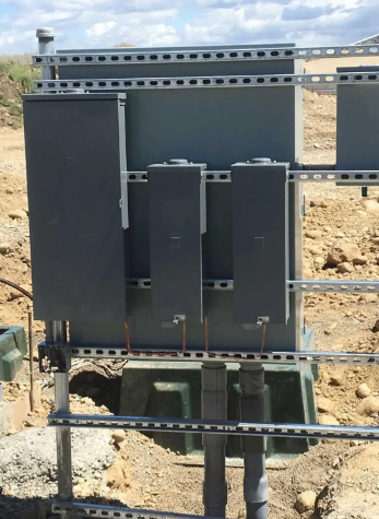 Black electrical control boxes mounted on a metal frame at a construction site