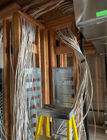 Electrical panel wiring in a construction site, with bundled white cables and metal breaker boxes between wooden studs.