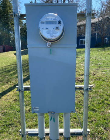 Outdoor electric meter in a gray utility cabinet mounted on metal poles in a grassy yard.