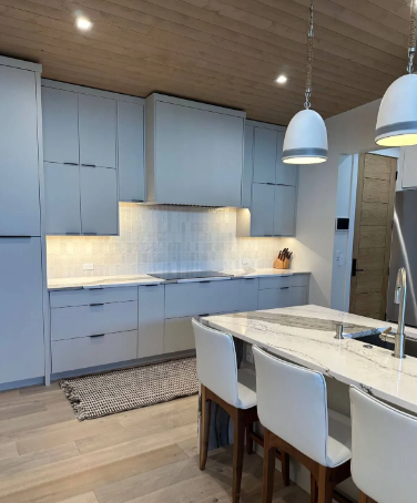 Modern kitchen with light gray cabinets, white island, wood ceiling, and pendant lights