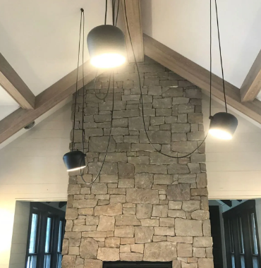 Stone fireplace wall with exposed wood beams and three hanging pendant lights in a vaulted room