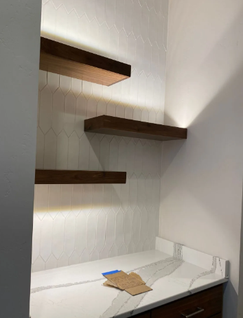 Minimalist bathroom with white vanity, hex tile wall, and floating wooden shelves.