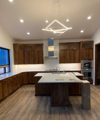 Modern kitchen with dark wood cabinets, large island, and geometric ceiling light in a bright open room