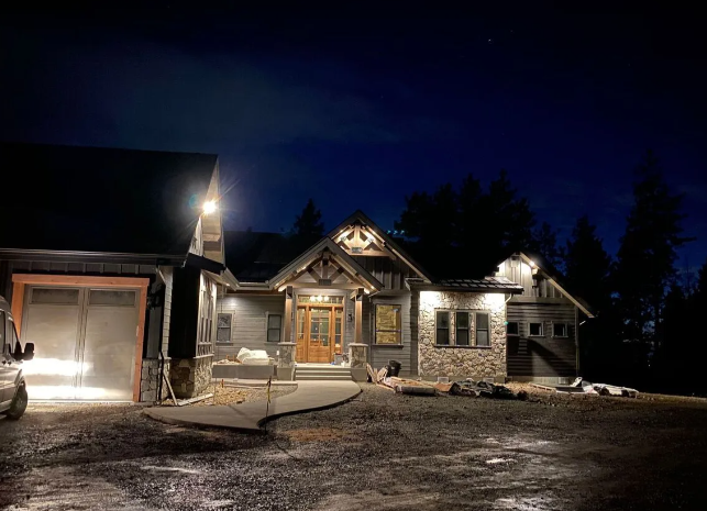 Snowy house exterior at night, warmly lit with a garage and stone façade under a dark blue sky