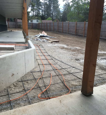 Patio under construction with concrete slab, orange cord, and lumber pile in a fenced yard