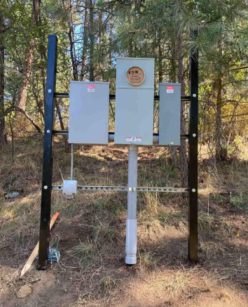 Outdoor electrical panel boxes on posts in a wooded area.