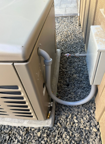 Outdoor HVAC unit with gray conduit running over gravel beside a wall