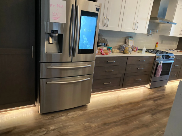 Modern kitchen with stainless steel fridge, dark cabinets, blue stove, and under-cabinet lighting