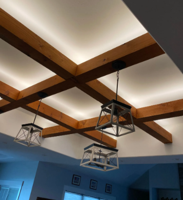 Ceiling with wooden beams, recessed lighting, and three hanging geometric pendant lights over a room.