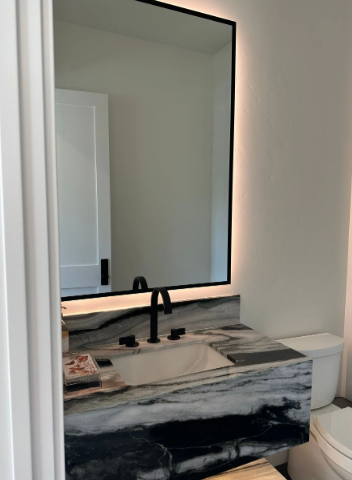 Bathroom vanity with black faucet, large mirror, marble countertop, and toilet beside it.