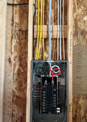 Open electrical breaker panel with exposed wiring in a stud wall cavity