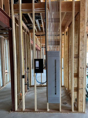 Unfinished house framing with an electrical panel and exposed wiring in a narrow hallway