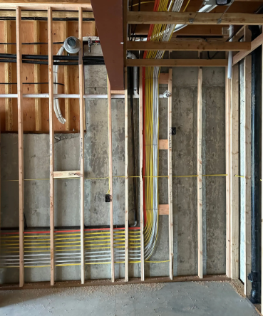 Interior construction framing with exposed wood studs, metal ducts, and electrical wiring in an unfinished wall