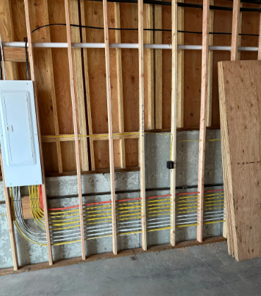 Unfinished interior wall framing with exposed studs, electrical wiring, and a plywood sheet leaning on the right