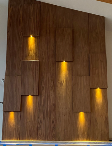Modern wood-paneled wall with four warm recessed lights and a blue LED strip at the base