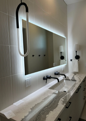 Modern restroom with long mirror, twin sinks, black faucets, and a wall-mounted light