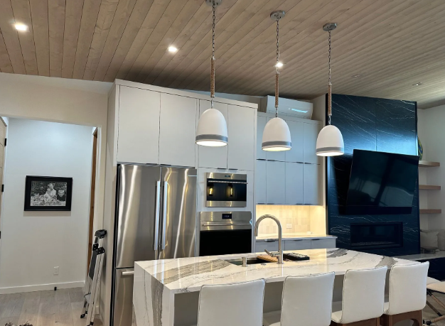 Modern kitchen with white island, pendant lights, stainless appliances, and a large black TV on the wall