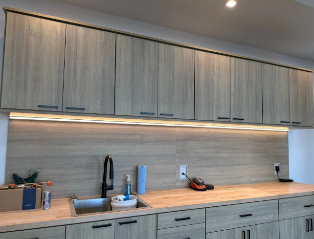 Modern kitchen with light wood cabinets, under-cabinet lighting, sink, and wood countertop.