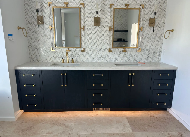 Dark navy double vanity with gold hardware, white countertop, and two mirrors on a herringbone tile wall.