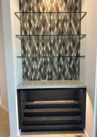 Built-in alcove with patterned wallpaper, glass shelves, and a dark cabinet below