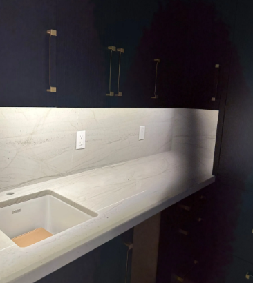 Modern kitchen with white quartz countertop, sink cutout, and dark cabinets in a dim room