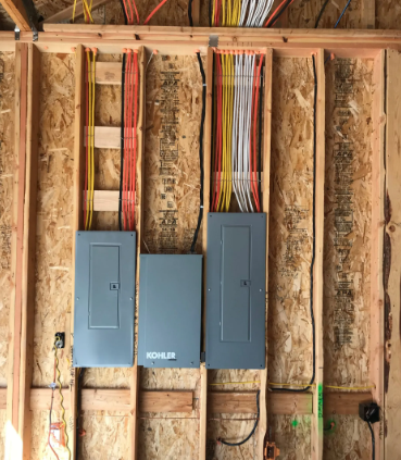Three blue electrical panels mounted on exposed wall studs with visible wiring in a framed interior wall