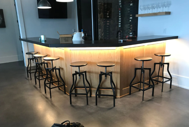 Modern bar with curved wood counter, black stools, and warm under-counter lighting in an empty room