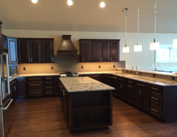 Modern kitchen with dark wood cabinets, granite island, pendant lights, and hardwood floors.