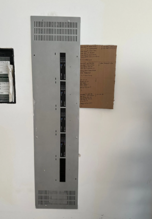 Wall-mounted electrical control panel next to a handwritten note on brown paper.