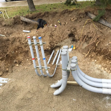 Outdoor construction trench with gray and white PVC pipes and fittings exposed in dirt
