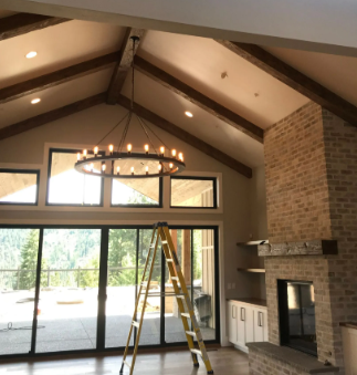 Living room with vaulted ceiling, chandelier, brick fireplace, tall windows, and a ladder in the center