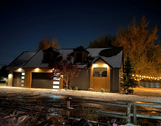 Snowy house exterior at night with warm lights glowing from windows and garage.