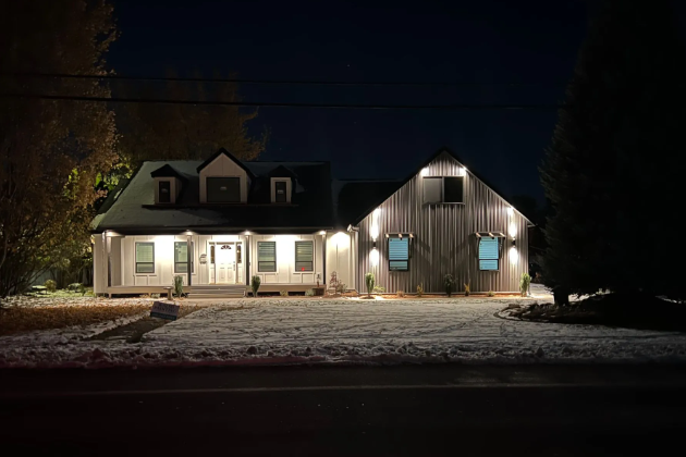 Snowy house exterior lit at night, with a porch and barn-style wing.