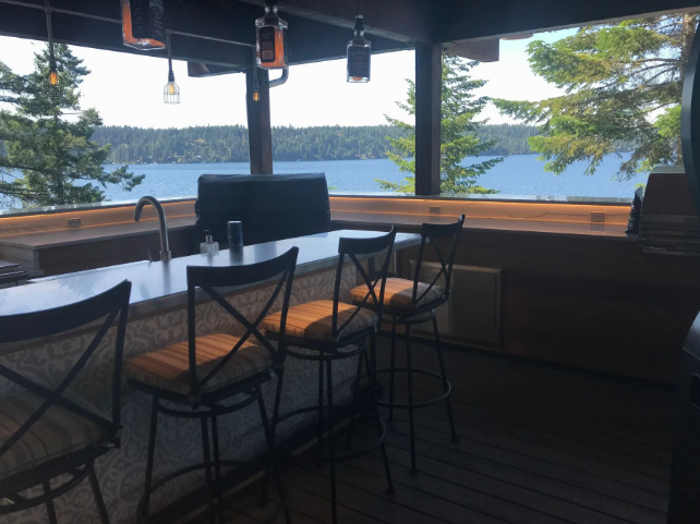 Lakeside restaurant patio with wooden tables, chairs, and large windows overlooking the water