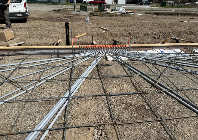 Rebar grid laid on gravel at a construction site, with a white vehicle in the background.