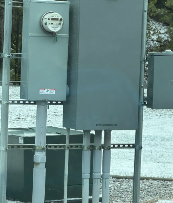 Electrical meter and utility boxes on a metal pole in a snowy outdoor area.