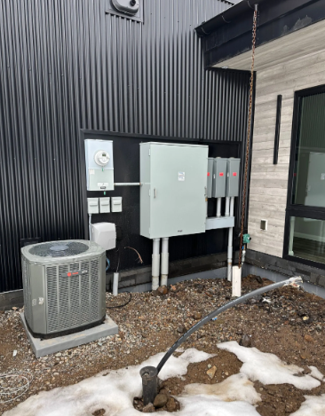 Outdoor HVAC and electrical equipment beside a building, with patchy snow and gravel ground.
