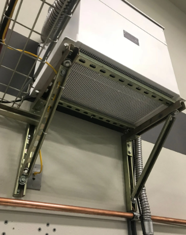 Industrial wall-mounted metal cabinet with vented panel and cables in a utility room